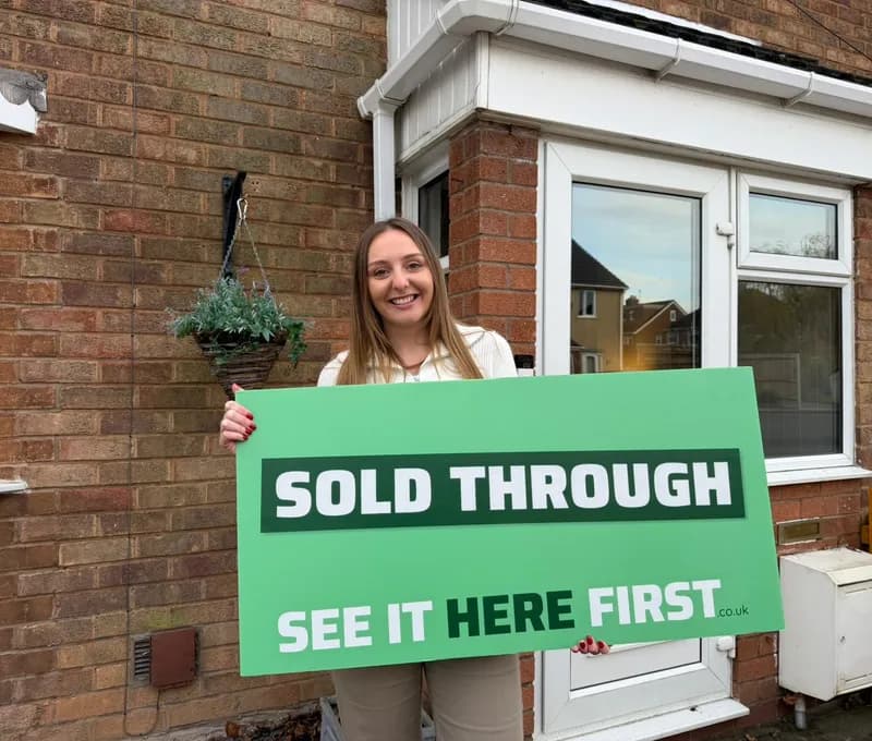 Homebuyer holding a Sold Through SEE IT HERE FIRST board
