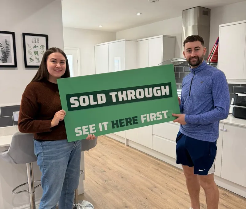 Seller who sold through SEE IT HERE FIRST holding a Sold Through SEE IT HERE FIRST board